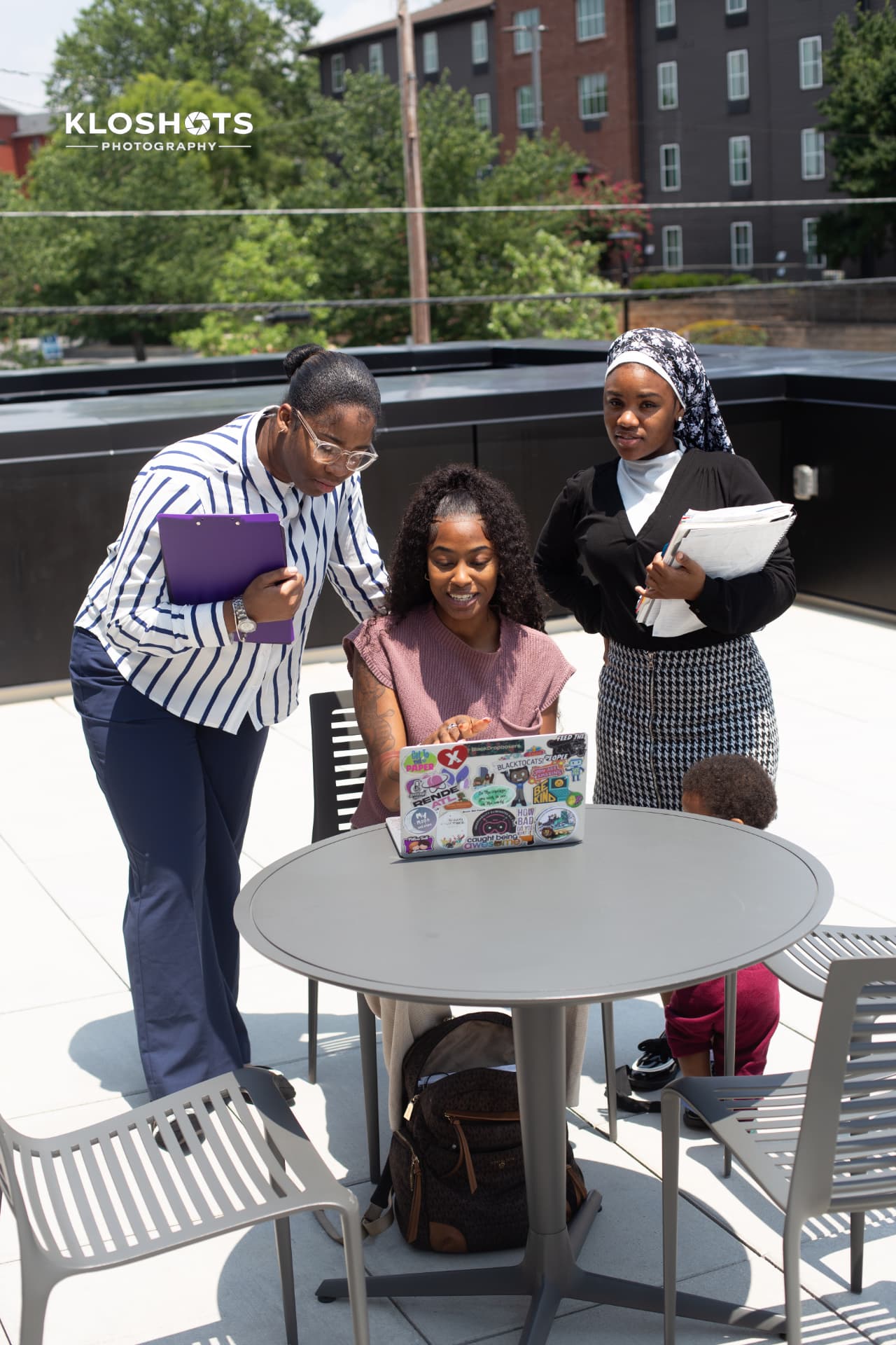 Students reviewing work on a laptop with an instructor on a rooftop terrace